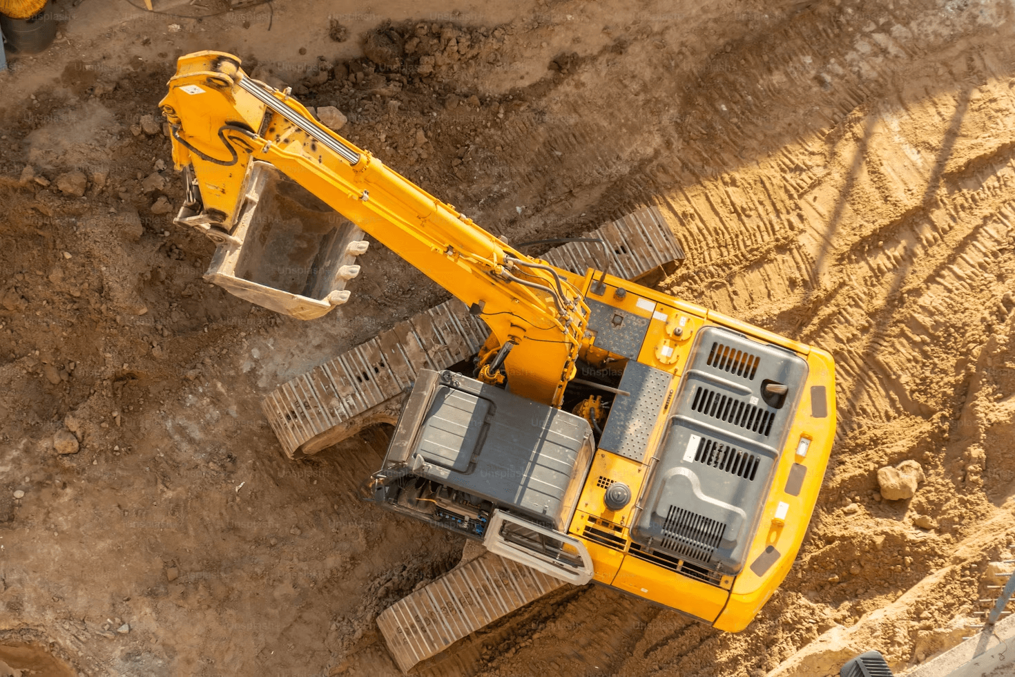 A tracked excavator working an open site, seen from above.